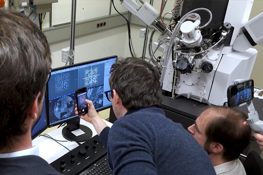 3 people positioned in front of a monitor screen. One person is photographing the QR code with his mobile phone. © TU Wien